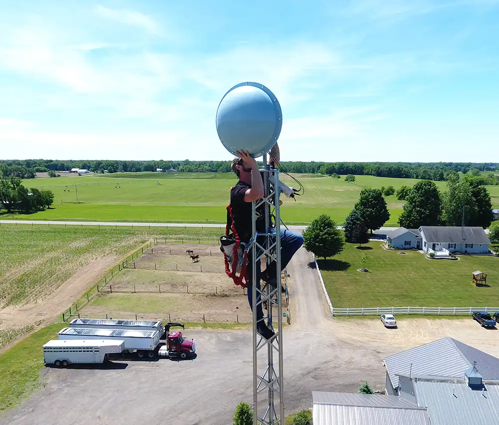 Technician climbing radio tower in middle of farmland